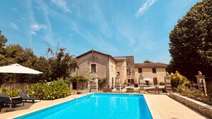 Una piscina con lettini, un edificio in pietra e cielo sereno.
