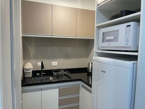A compact kitchen with white cabinets, a microwave, and a coffee maker. - Apartment in the Refinatto Building in downtown Curitiba, near Shopping Estação. (Curitiba)