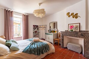 Ein Schlafzimmer mit Bett, Vorhängen, einer Pendelleuchte, einem Kamin, einem Spiegel und einer Kommode.