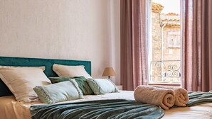 Una cama bien tendida con un cabecero verde azulado, un edredón verde y una toalla enrollada.