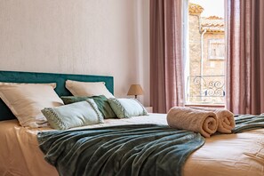 Una cama bien tendida con un cabecero verde azulado, un edredón verde y una toalla enrollada.