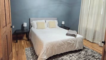 A bedroom with a bed, bedside tables, a nightstand, a rug, and a door.
