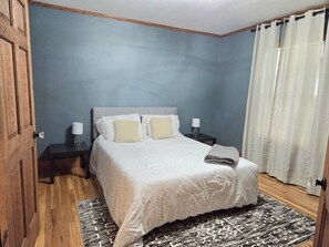 A bedroom with a bed, bedside tables, a nightstand, a rug, and a door.