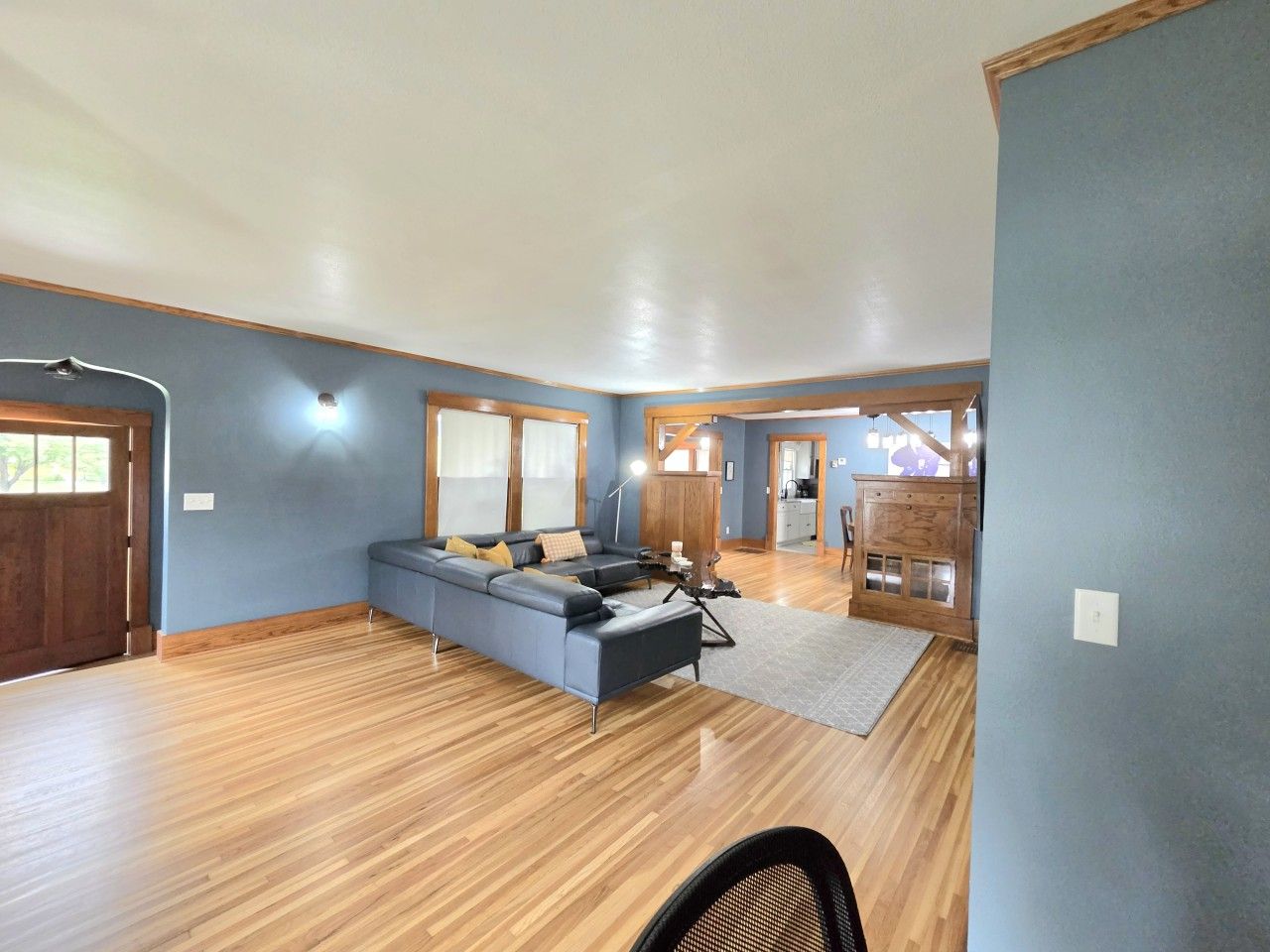 A spacious living area with a large sofa, wooden flooring, and a view of the kitchen.