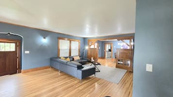A spacious living area with a large sofa, wooden flooring, and a view of the kitchen.