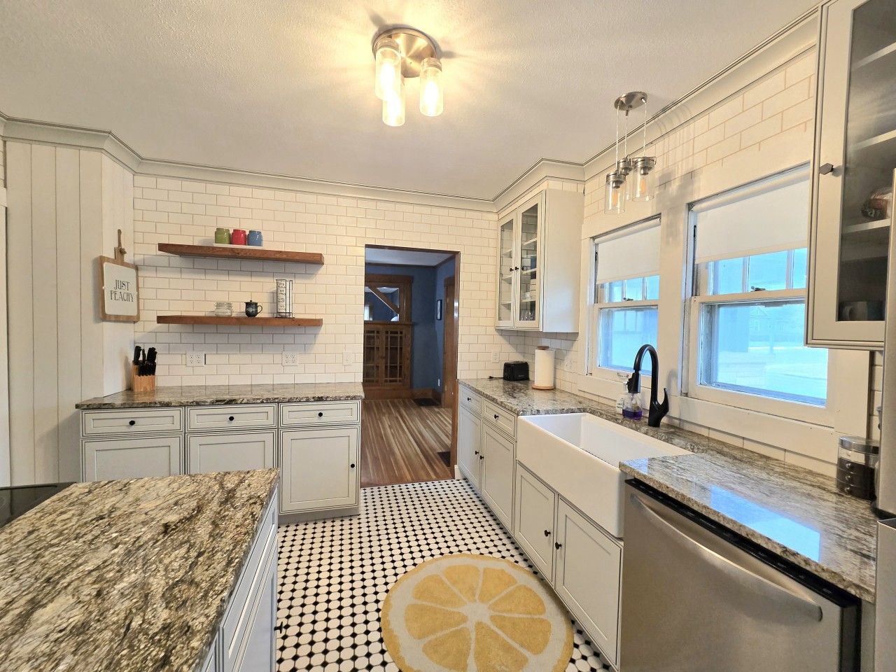 A kitchen with white cabinets, a granite countertop, a black and white patterned floor, and a window with a view.