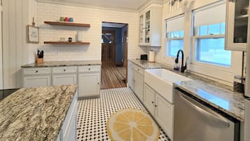 A kitchen with white cabinets, a granite countertop, a black and white patterned floor, and a window with a view.