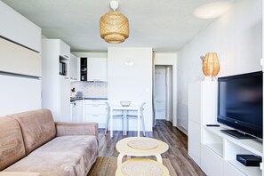 A modern living room with a sofa, a TV, and a dining area with a table and chairs. - Le Cocon Ensoleillé - Avec vue mer (Le Barcarès)