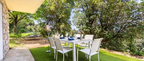 An outdoor dining area with a table set for four, surrounded by white chairs, under a canopy.