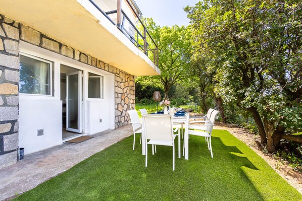 Une maison moderne avec une façade en pierre, un balcon et une pelouse bien entretenue, agrémentée d’une table et de chaises pour les repas.