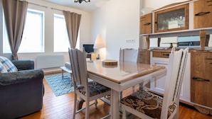Un soggiorno moderno con tavolo da pranzo, sedie, un divano, una TV e un angolo cottura con mobili in legno e una finestra.