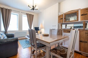 A modern living room with a dining table, chairs, a sofa, a TV, and a kitchen area with wooden cabinets and a window. - Le Nid de Boulogne - À 2 km de la plage (Boulogne-Sur-Mer)