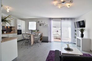 Eine moderne Küche mit Essbereich, ein Wohnzimmer mit Sofa und Couchtisch sowie ein an der Wand befestigter Fernseher.