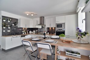 Eine moderne Küche mit weißen Schränken, einer Marmor-Spritzschutzwand und einem Essbereich mit Tisch und Stühlen für zwei Personen.