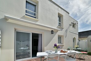 Eine Terrasse mit Tisch und Stühlen, eine Glastür und ein kleiner Gartenbereich.