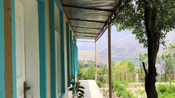 A covered outdoor area with a door, potted plants, and a view of a mountainous landscape. - Asqur Bassi (Mekhtar)