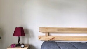 A bedroom with a wooden headboard, a bedside table with a lamp, and a small decorative item. - Asqur Bassi (Mekhtar)