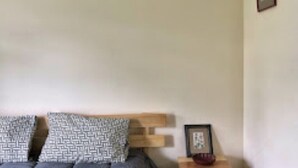 A room with a bed, pillows, a wooden headboard, a framed picture, and a small table with a vase. - Asqur Bassi (Mekhtar)