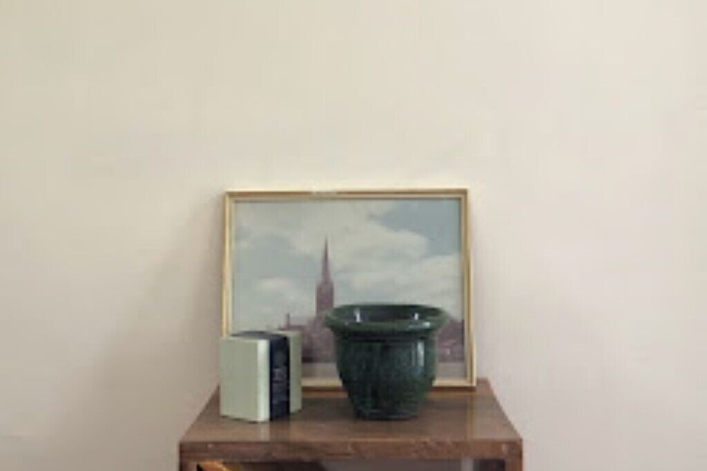 A framed picture of a building, a green vase, and a small object on a wooden surface.