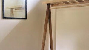 A room with a wooden bed frame, a framed picture on the wall, and a window with natural light. - Asqur Bassi (Mekhtar)