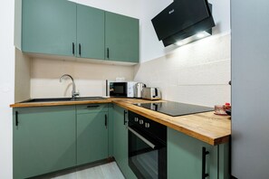 Una cocina compacta con armarios verdes, un microondas, un tostador y una encimera de madera.