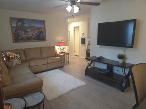 Ein Wohnzimmer mit einer Couch, einem Couchtisch, einem Fernseher, einer Lampe und einem Bild an der Wand.