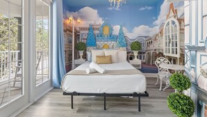 Ein Schlafzimmer mit einem großen Bett, einer Chandelüster, einer Blick auf eine Wandmalerei mit Schlossdarstellung und einem Balkon mit Geländer.