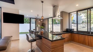 A modern kitchen with a central island, bar stools, a flat-screen TV, and large windows. - Casa Brisa, Playa del Carmen (Playa del Carmen)