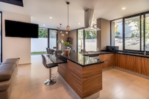 A modern kitchen with a central island, bar stools, a flat-screen TV, and large windows. - Casa Brisa, Playa del Carmen (Playa del Carmen)