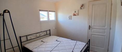 A bedroom with a bed, a window, a door, and a small stool.