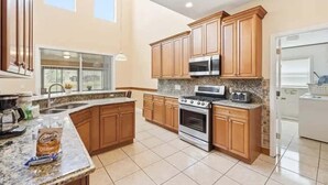 A spacious kitchen with wooden cabinets, a large island, stainless steel appliances, and a window providing natural light. - Family Home with Private Pool Near Disney (Kissimmee)