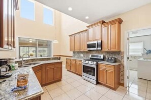 A spacious kitchen with wooden cabinets, a large island, stainless steel appliances, and a window providing natural light. - Family Home with Private Pool Near Disney (Kissimmee)