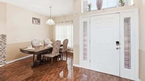 A dining area with a table and chairs, a chandelier, a white door with a decorative panel, and a window with plants. - Family Home with Private Pool Near Disney (Kissimmee)