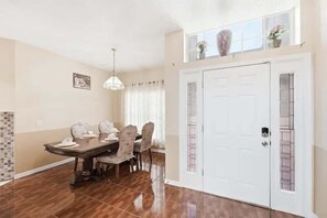 A dining area with a table and chairs, a chandelier, a white door with a decorative panel, and a window with plants. - Family Home with Private Pool Near Disney (Kissimmee)