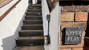 A staircase leading to a door labeled 'UPPER FLAT' with a brick wall and a white wall on either side. - Charming, spacious and full of natural light 2-story flat in central Saxmundham. (Saxmundham)