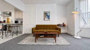 A living room with a sofa, coffee table, and a painting on the wall. - Charming, spacious and full of natural light 2-story flat in central Saxmundham. (Saxmundham)