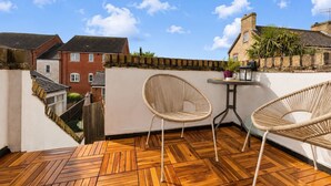 A wooden deck with two wicker chairs and a small table, overlooking a residential area with brick houses and a clear sky. - Charming, spacious and full of natural light 2-story flat in central Saxmundham. (Saxmundham)