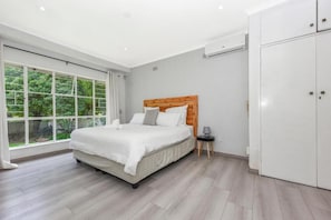 Ein Schlafzimmer mit einem großen Bett, einem Kleiderschrank und einem Fenster mit Blick ins Grüne.