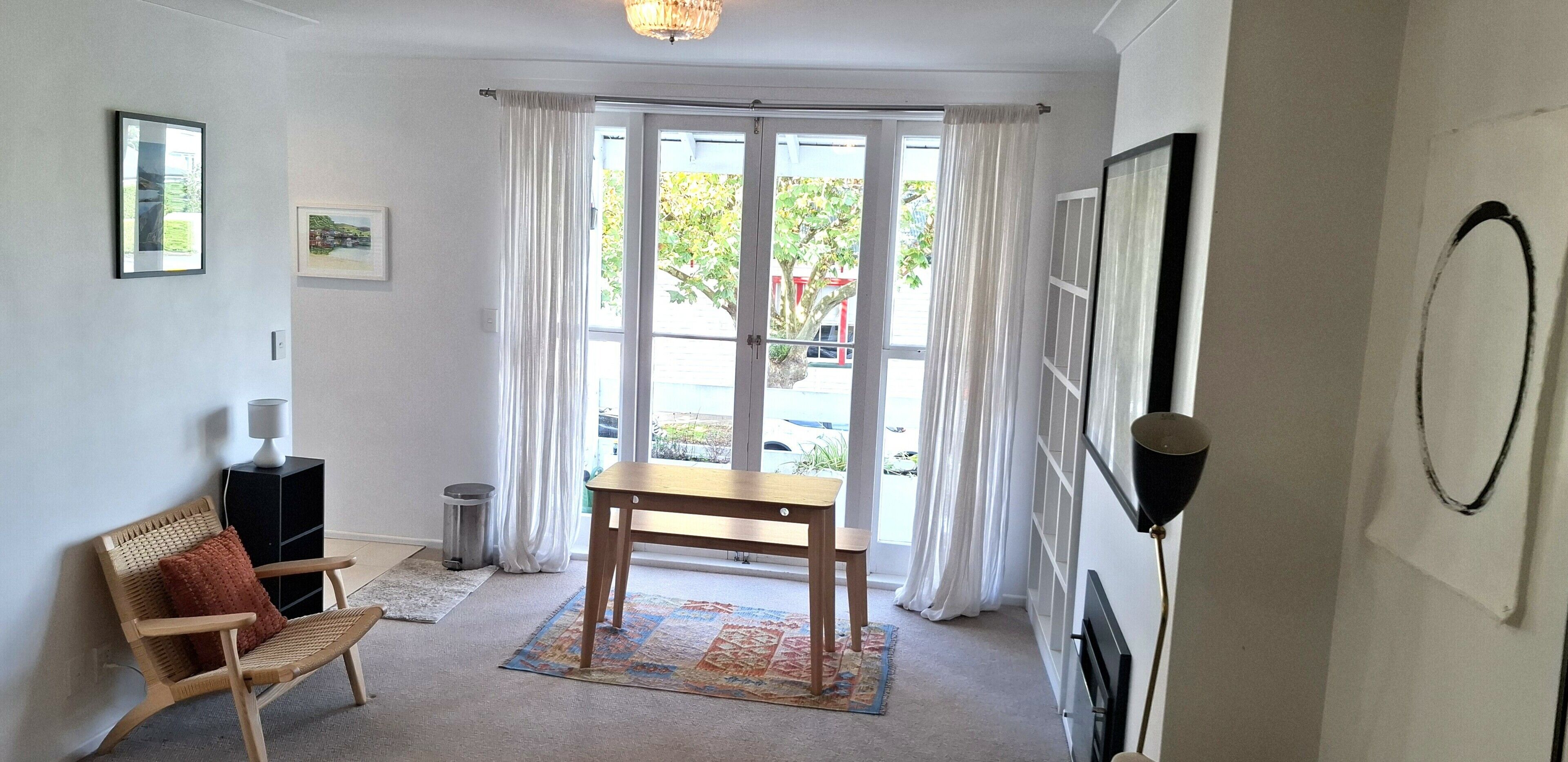 A room with a wooden table, a chair, a lamp, a rug, and a window with curtains.