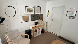 Ein Zimmer mit Schreibtisch, Stuhl und Tür. An der Wand hängen Bilder in Rahmen.