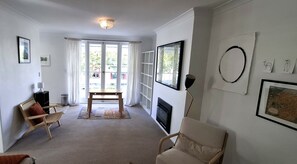Un salon avec une cheminée, un canapé, un fauteuil, une table basse et une grande fenêtre avec des rideaux.