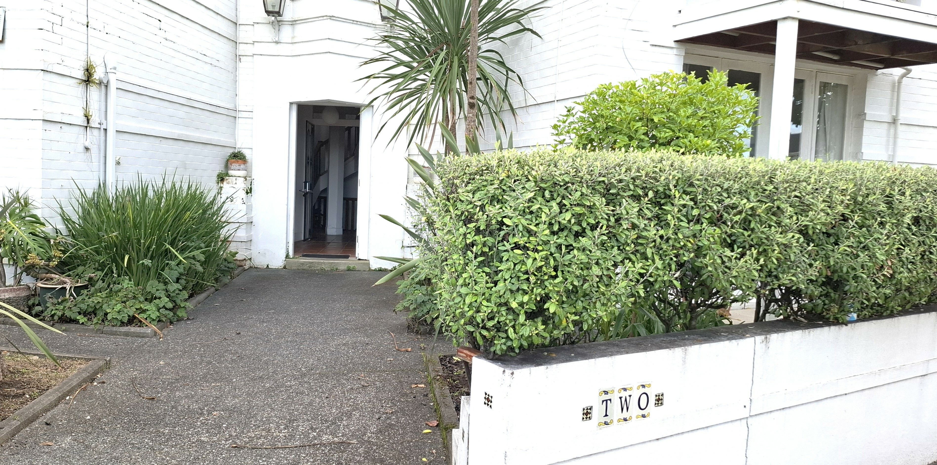 A white building with a paved entrance and a hedge in front.
