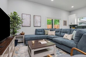 Ein Wohnzimmer mit Ecksofa, Couchtisch, Fernseher und einer Pflanze.