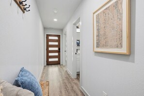 Ein Flur mit einer Holztür, einem gerahmten Kunstwerk an der Wand und einem Teppich mit Struktur auf dem Boden.