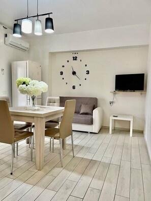 A modern living room with a dining area, a sofa, a TV, and a clock on the wall. - To complete (Agropoli)
