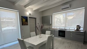Una cocina moderna con estufa integrada, un amplio ventanal y una zona de comedor con mesa y sillas blancas.