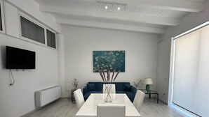 Una sala de estar moderna con una mesa de comedor blanca, un sofá azul y un cuadro en la pared.