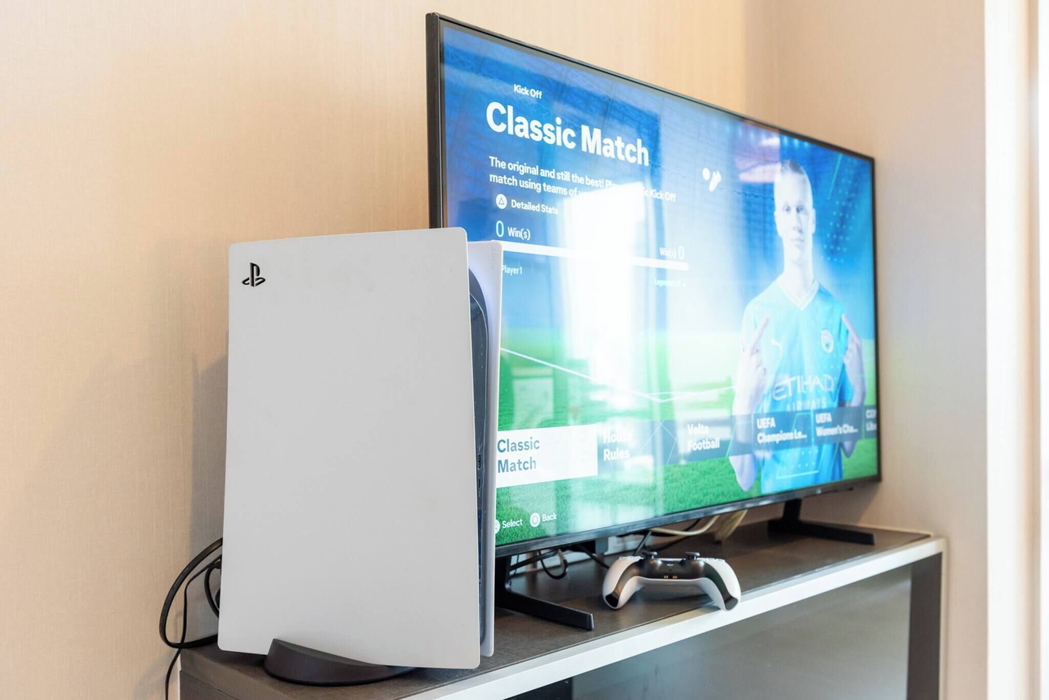 Una consola PlayStation 5 junto a un televisor que muestra un partido de fútbol.