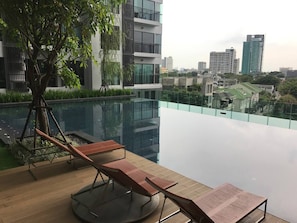 Un bâtiment moderne doté d’une piscine sur le toit, de chaises longues et d’un arbre.