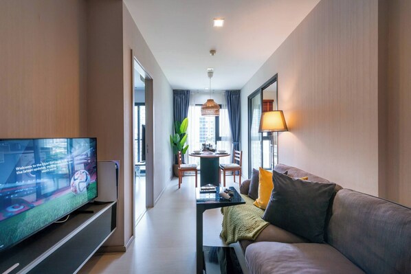A modern hotel room with a flat-screen TV, a sofa, a dining table, and a large window.